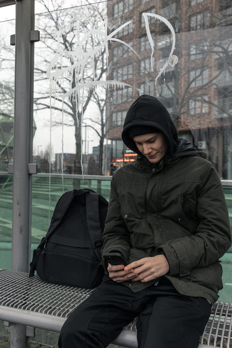 Jongere met smartphone in bushokje